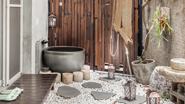 Una terraza de madera con un jacuzzi, escalones de piedra y una valla de bambú.
