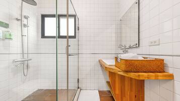A bathroom with a glass-enclosed shower, a wooden vanity with a basket, and a mirror above the sink.