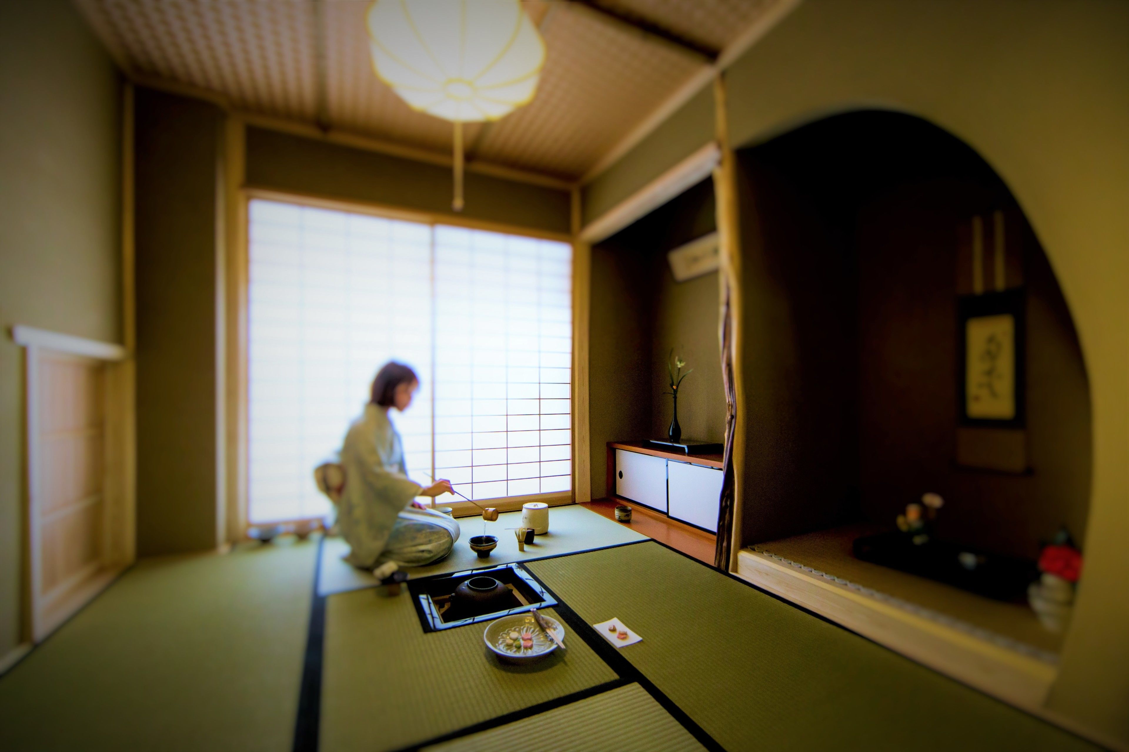 A traditional Japanese room with tatami flooring, a low table with a tea set, and a sliding door.