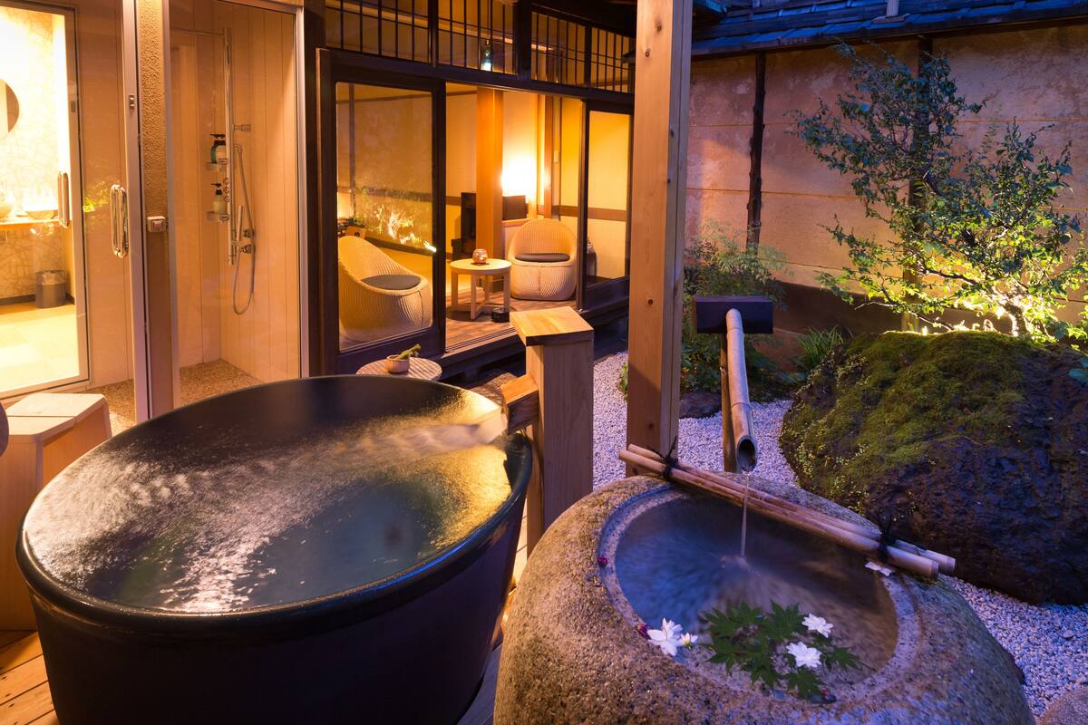 A traditional Japanese onsen with a large hot spring, wooden seating, and a stone basin with a bamboo rake.