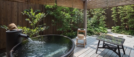 A hot tub on a wooden deck with a bamboo fence and greenery in the background.