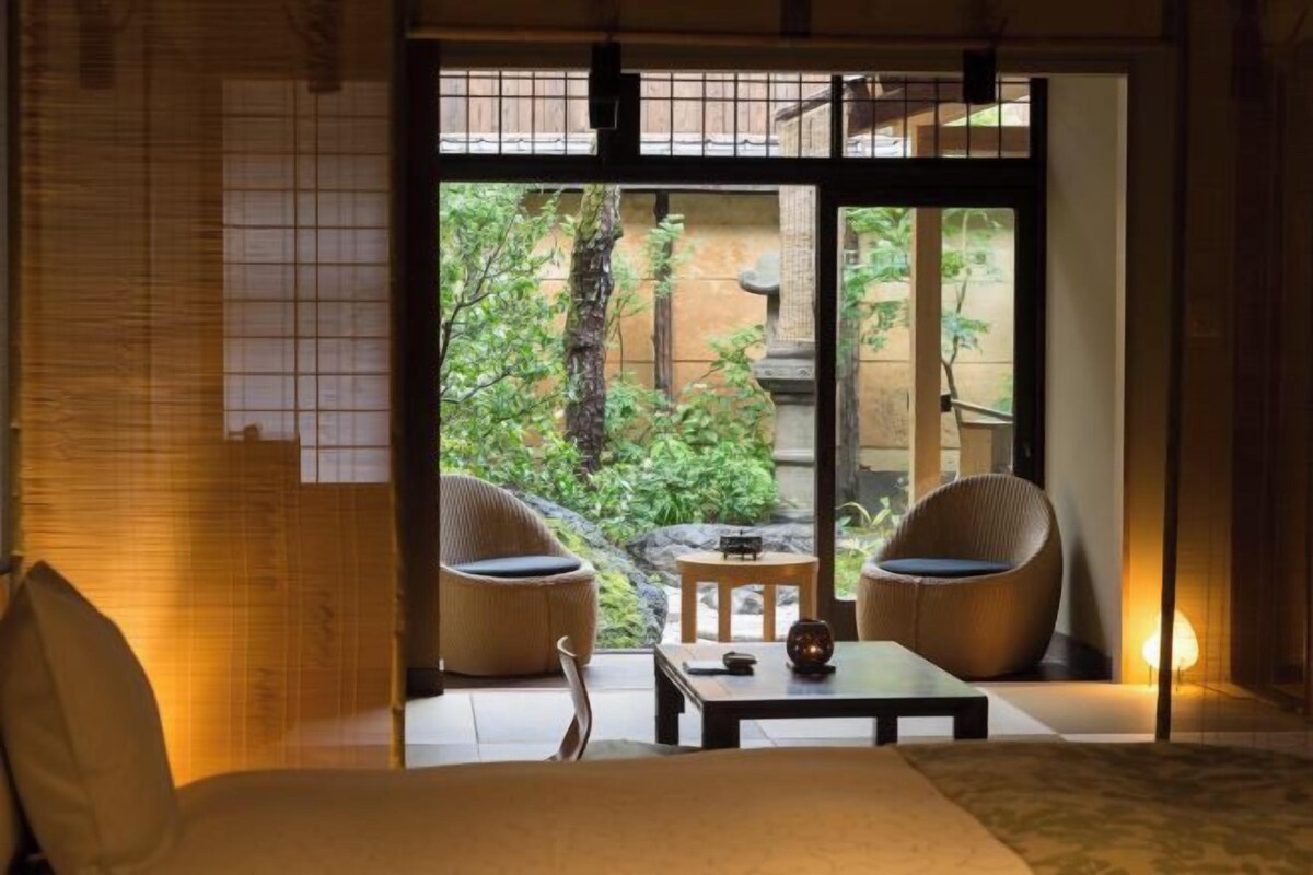 A traditional Japanese-style room with tatami flooring, a low table, two cushioned chairs, and a sliding door leading to a garden.
