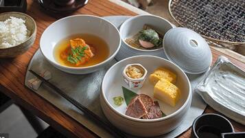 Presentació tradicional de menjar japonès amb diversos plats, com ara arròs, sopa i carn, damunt un taula de fusta.
