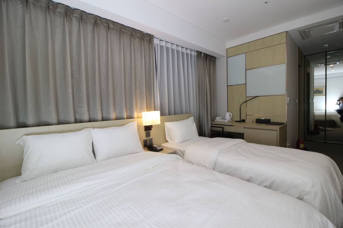 A hotel room with two beds, a desk, a chair, a lamp, and a mirror.