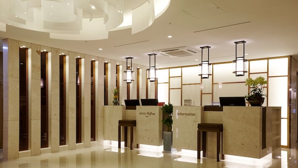 Zona de recepción de hotel con diseño moderno, que incluye un mostrador de mármol, un área de estar y un amplio mostrador de información.