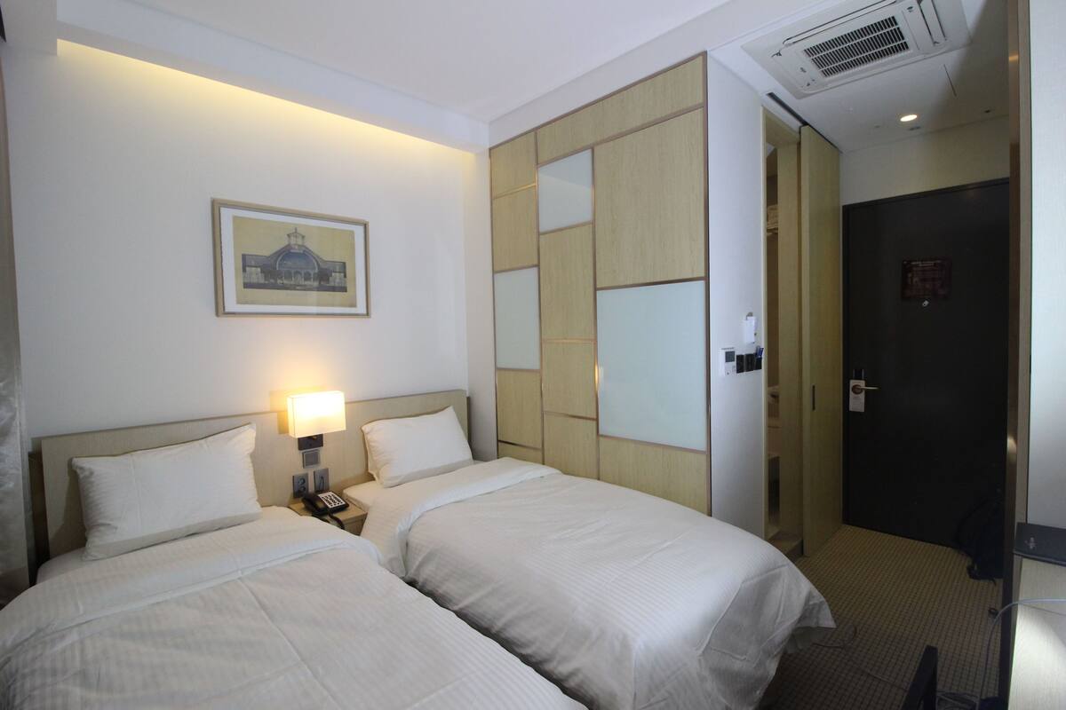 A hotel room with two beds, a nightstand with a lamp, a framed picture on the wall, and a wardrobe with mirrored doors.