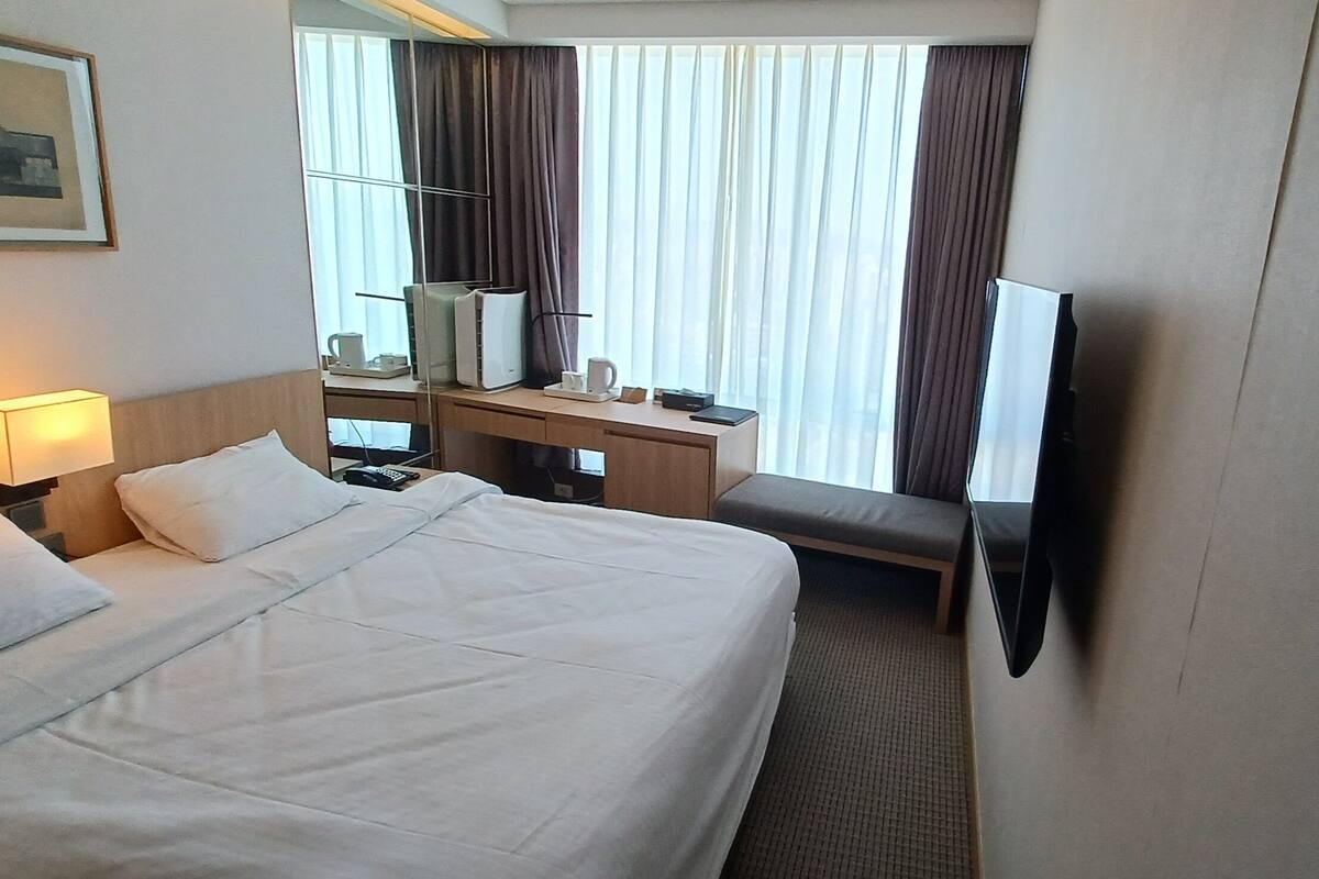A hotel room with a large bed, a desk with a computer, a TV, and a window with curtains.