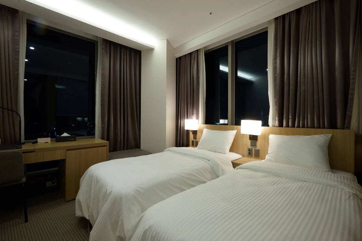 A hotel room with two beds, a desk, and a nightstand.