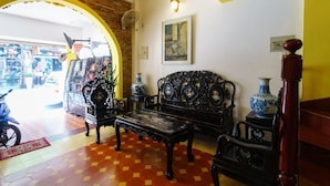 Une pièce avec un mur en briques, une arche jaune, un canapé noir, une table en bois et un vase décoratif.
