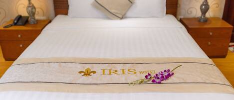 Una cama de hotel con una colcha que muestra el logotipo del HOTEL IRIS y un símbolo de lis.