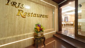 A reception area with a marble wall displaying the name "IRIS Restaurant" and a small table with a floral arrangement. - Iris Hotel Danang (Da Nang)