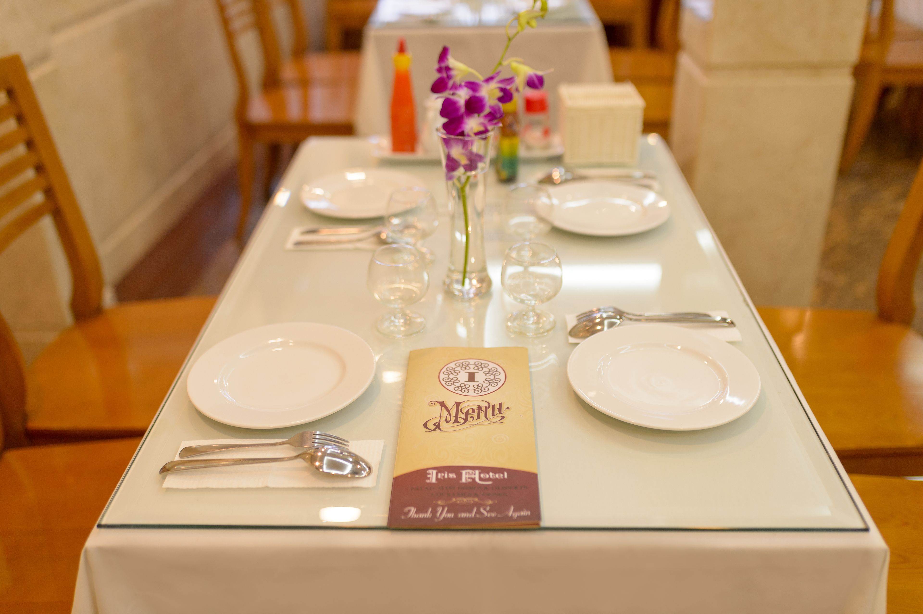 A dining table set with white plates, cutlery, and a menu.