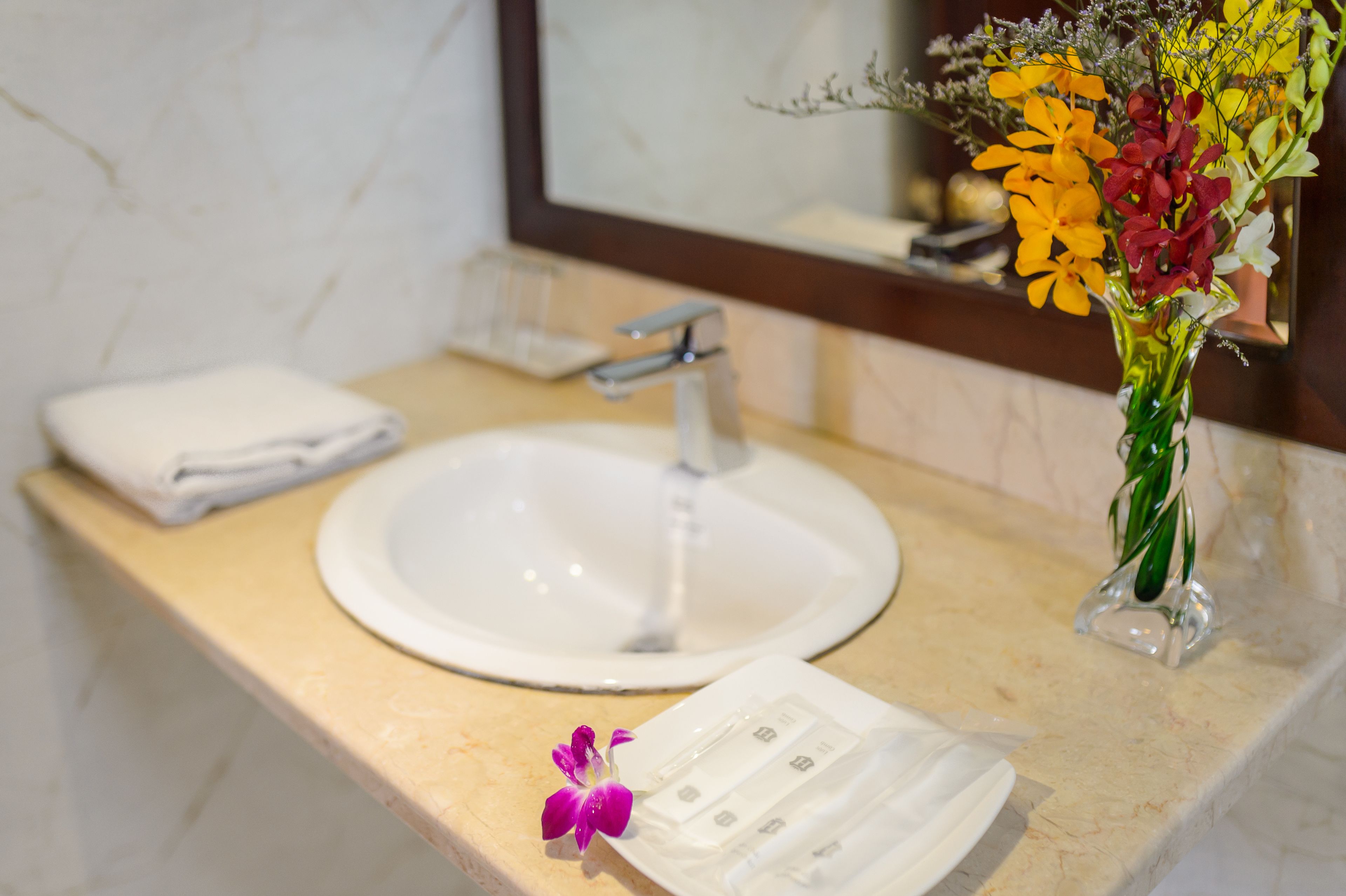 A bathroom sink with a mirror above it, a towel, and a vase with flowers.