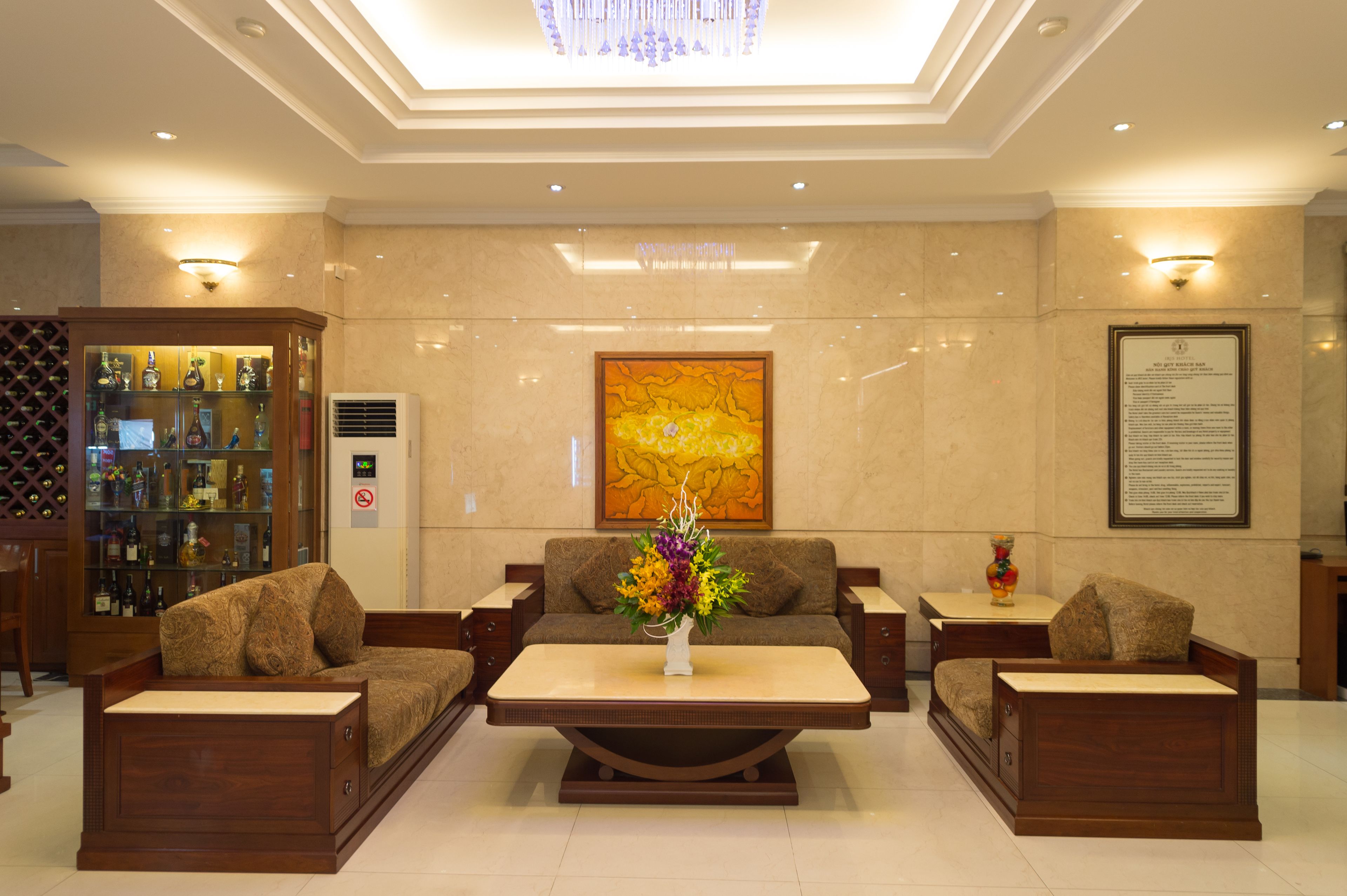 A lobby with a sofa set, a coffee table, a decorative vase, a wall-mounted artwork, and a display cabinet with bottles.