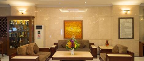 A lobby with a sofa set, a coffee table, a decorative vase, a wall-mounted artwork, and a display cabinet with bottles.