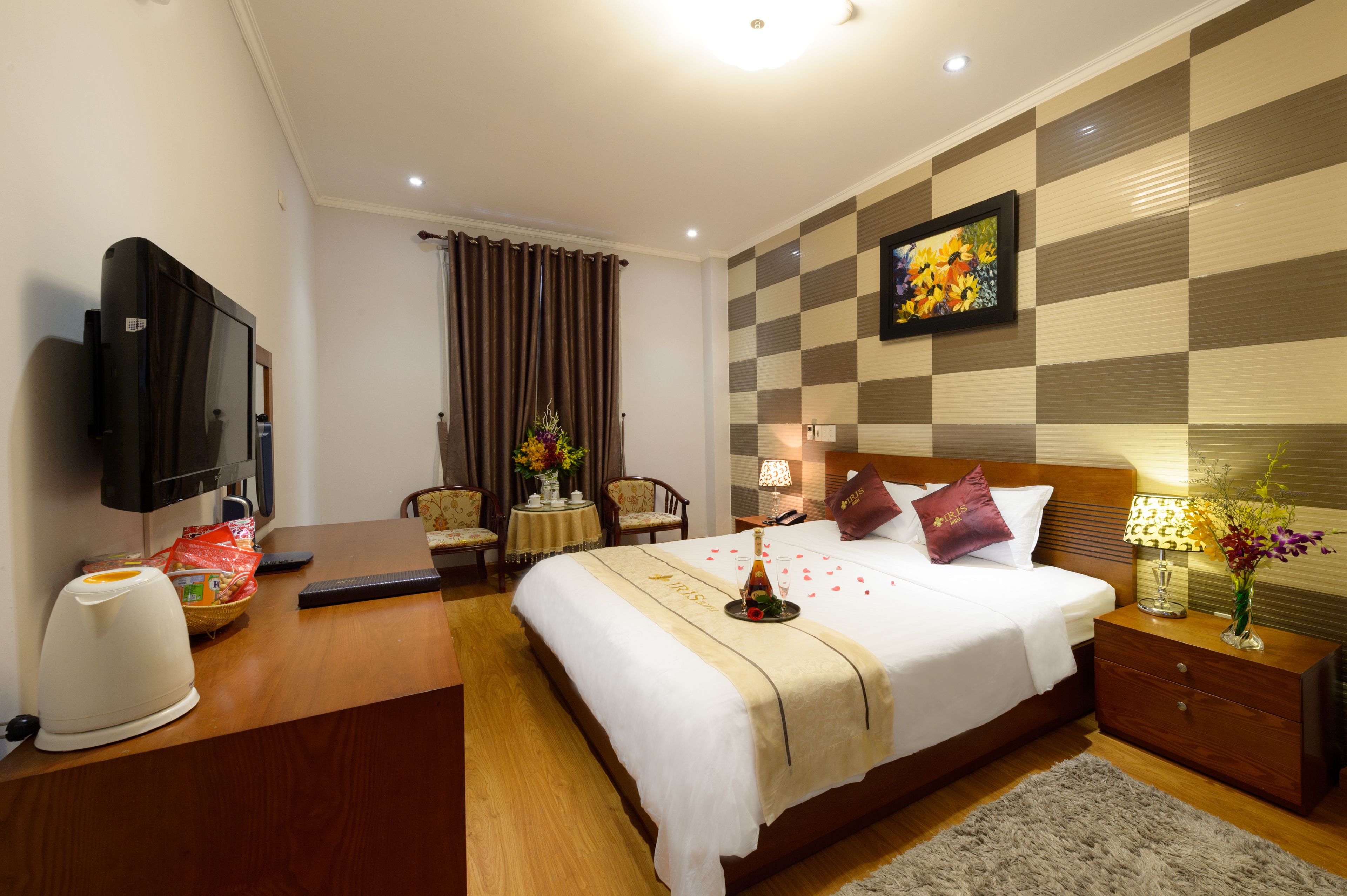 Habitación de hotel con cama, mesitas de noche, televisor, escritorio y una silla, además de hervidor.