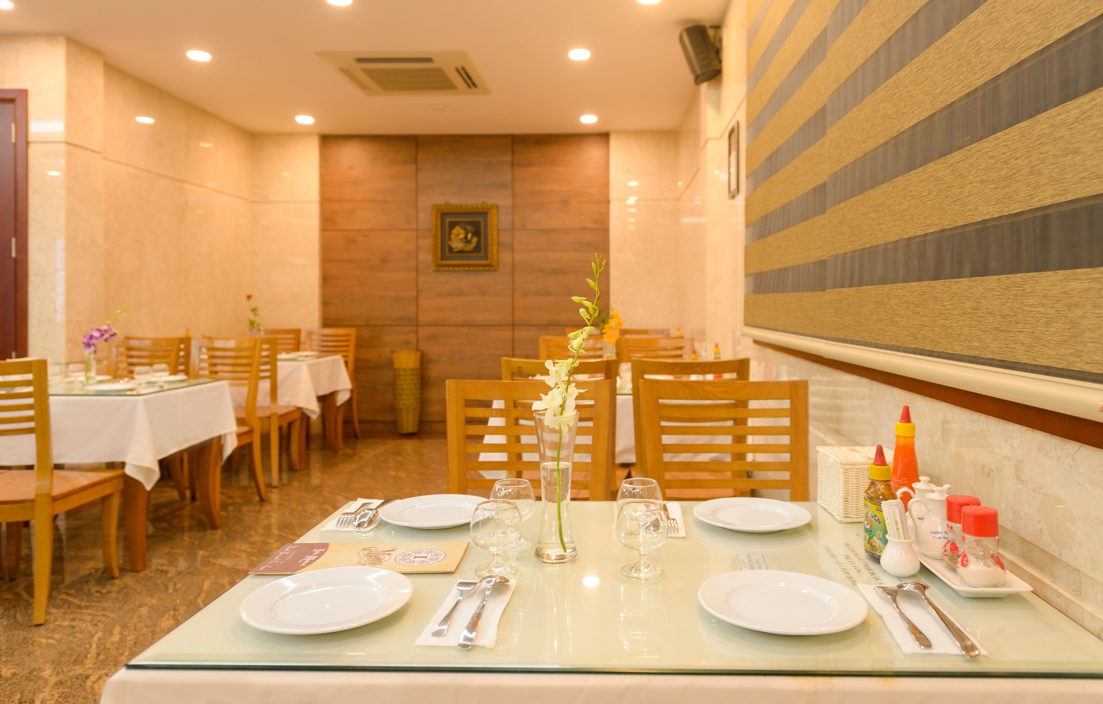 A dining area with tables set for two, each with plates, cutlery, and a vase of flowers.
