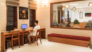 A hotel reception area with a wooden desk, two monitors, a seated person, a red bench, and a large mirror reflecting the interior. - Iris Hotel Danang (Da Nang)
