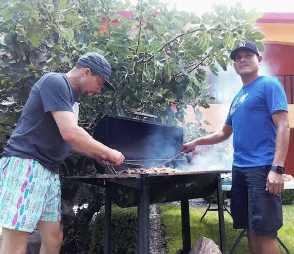 Deux personnes qui font un barbecue à l’extérieur, avec un gril et une table en arrière-plan.