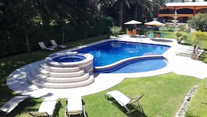 A swimming pool with a hot tub, surrounded by lawn chairs and umbrellas.