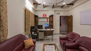 Een woonkamer met twee leren banken, een salontafel met kranten, een bureau met een computer en een printer, en een plafondventilator.