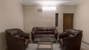 Een kamer met een glazen salontafel, twee bruine leren banken, een houten deur en een klein raam met zonwering.