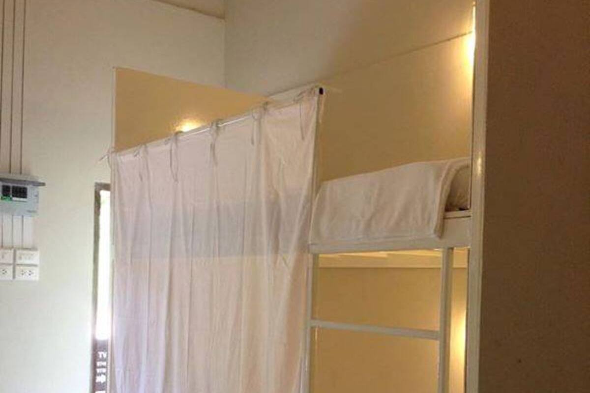 A bunk bed with a white mattress and a ladder, a white curtain, and a light switch on the wall.