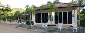 A building with a tiled roof, large windows, and outdoor seating with white chairs and tables. - The Best Hostel (Koh Tao)