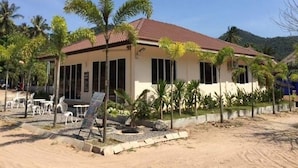 A two-story building with a red-tiled roof, surrounded by palm trees and a sandy ground. - The Best Hostel (Koh Tao)