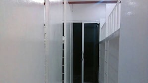 A narrow hallway with white walls and a tiled floor, leading to a door with a glass panel. - The Best Hostel (Koh Tao)