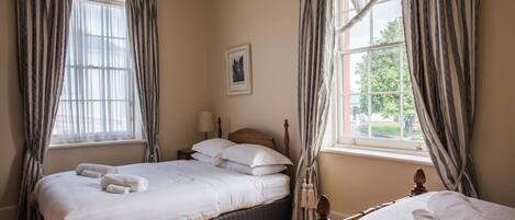 A bedroom with a large bed, two bedside tables, a window with curtains, and a view of the outside.