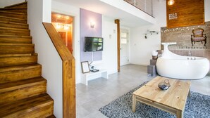 A spacious living area with a wooden staircase, a large white bathtub, and a television mounted on the wall.