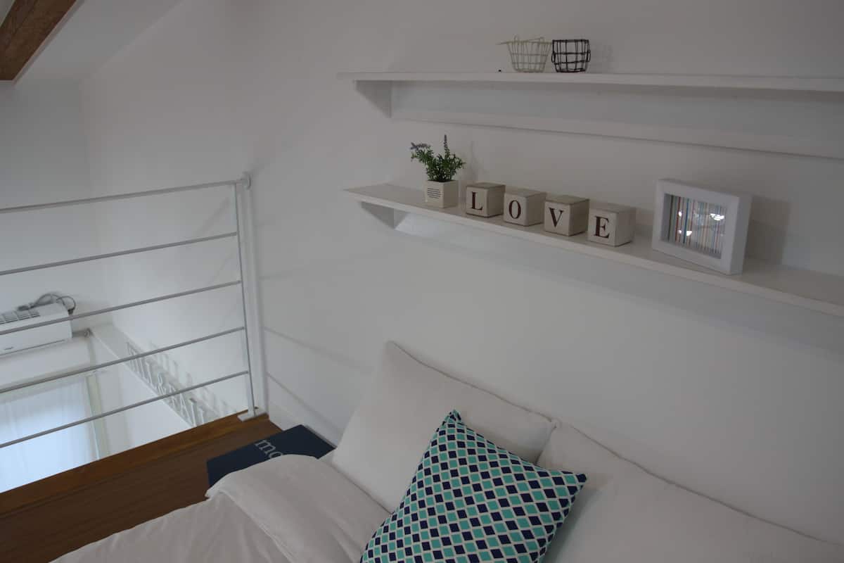 Een slaapkamer met een bed, een raam met uitzicht en planken met decoratieve spullen.