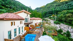 A hotel with a pool, wooden deck, and a view of a river and forest.