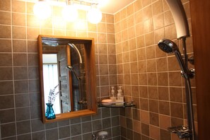 A bathroom with a shower, a mirror, and a shelf with toiletries. - Hill & Falls House (Gapyeong)