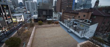 A rooftop terrace with a wooden deck, brick planters, and a cityscape view.