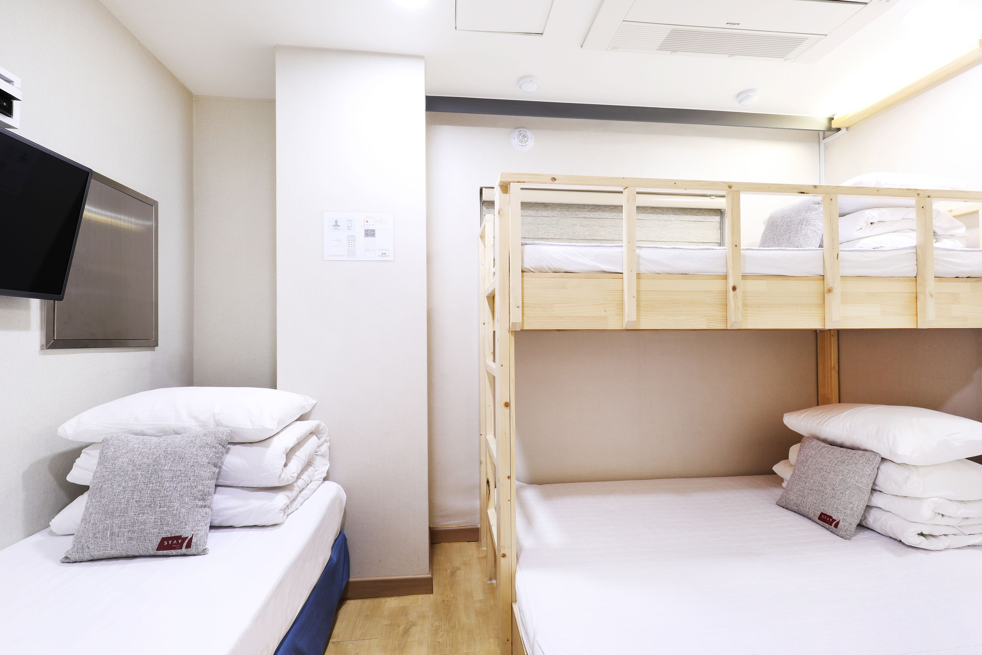 A hotel room with a bunk bed, a single bed, and a flat-screen TV mounted on the wall.
