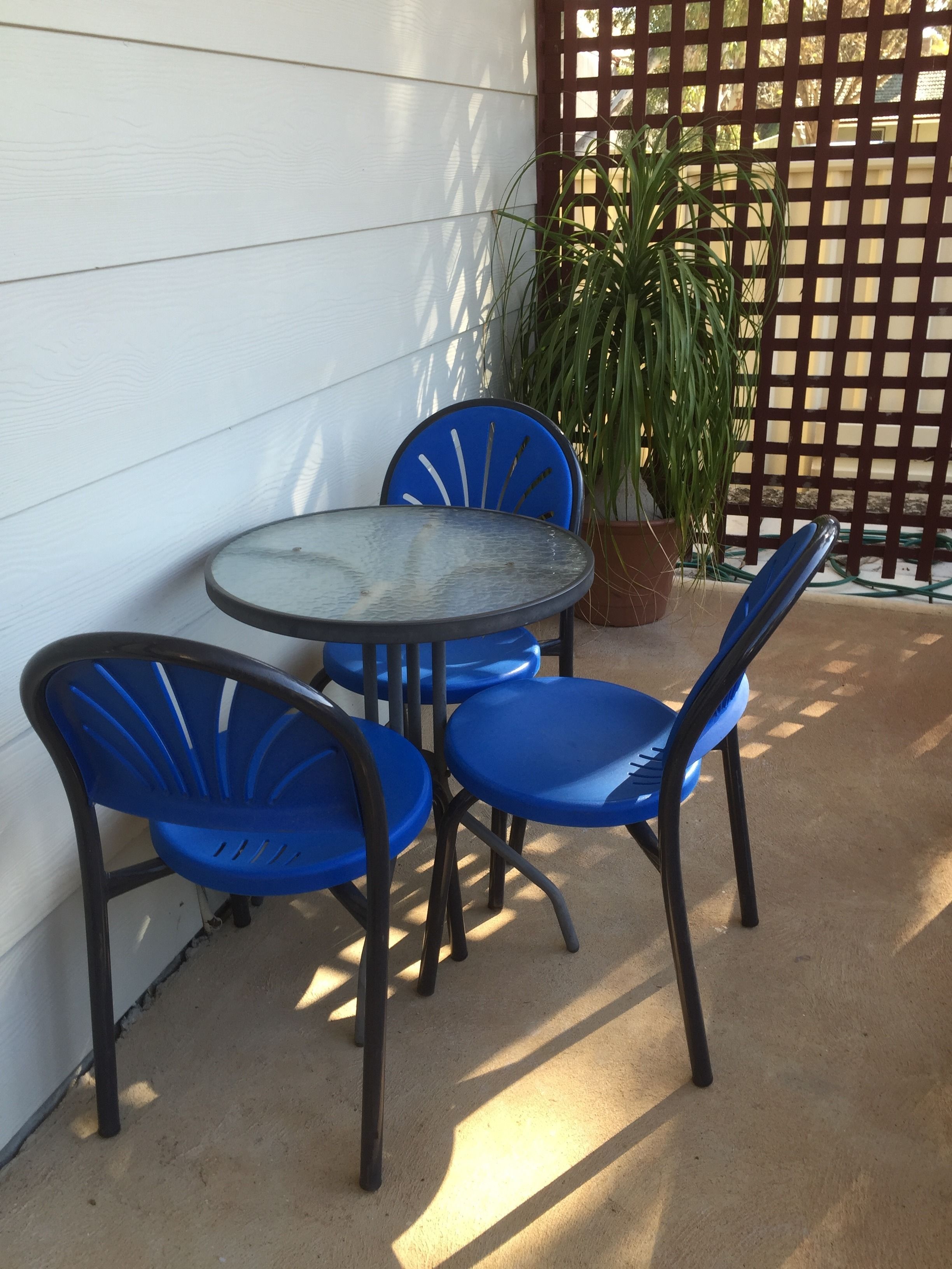 Una pequeña zona de estar al aire libre con una mesa redonda y cuatro sillas azules.