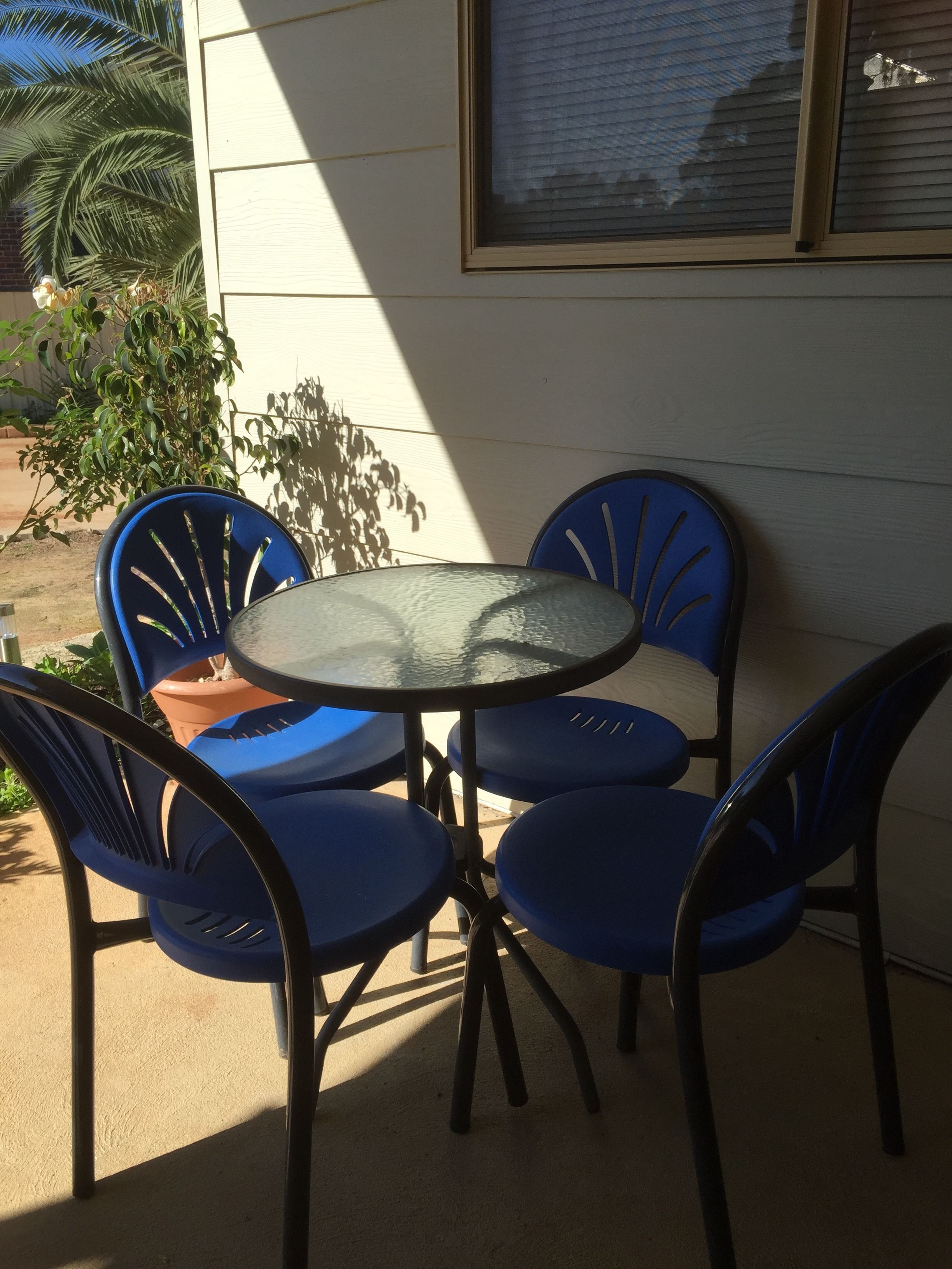 Une table ronde en verre, accompagnée de quatre chaises bleues.