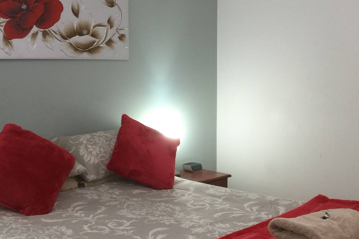 A neatly made bed with red pillows, a red throw blanket, and a folded towel on the bed.