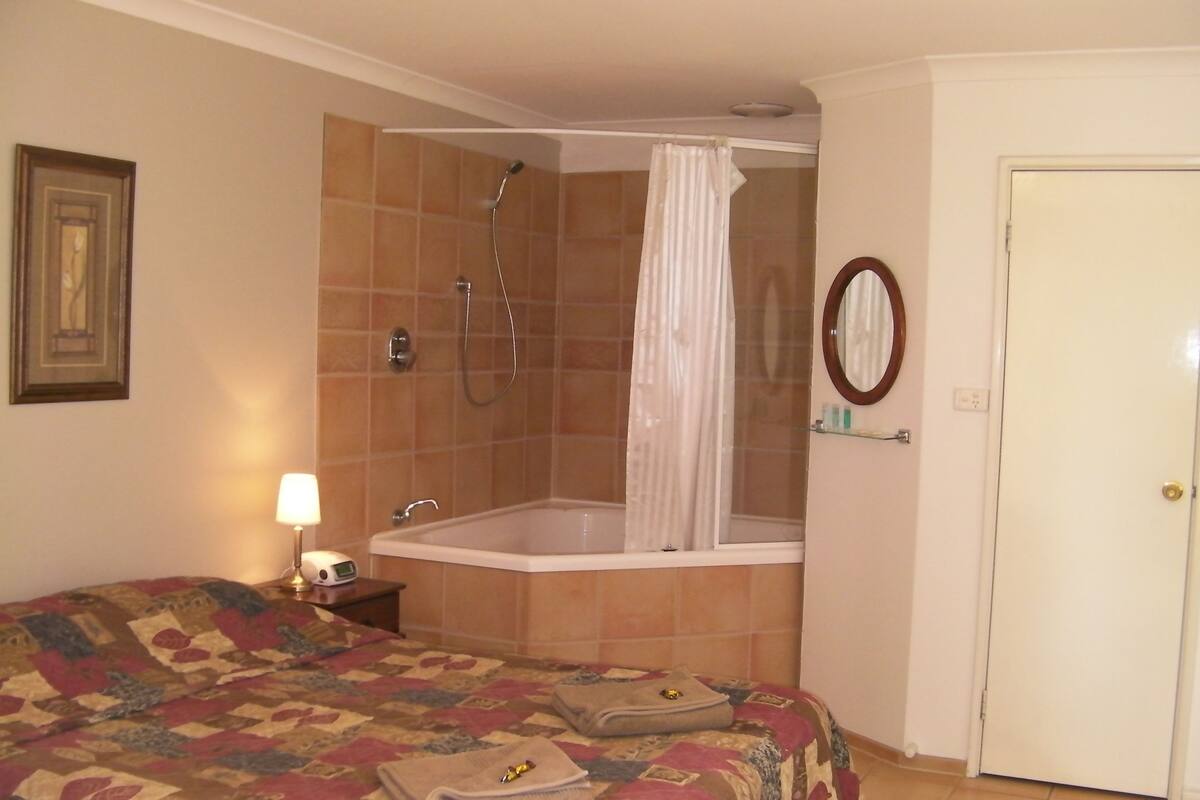 A hotel room with a bed, a bathroom with a shower, a toilet, and a door.