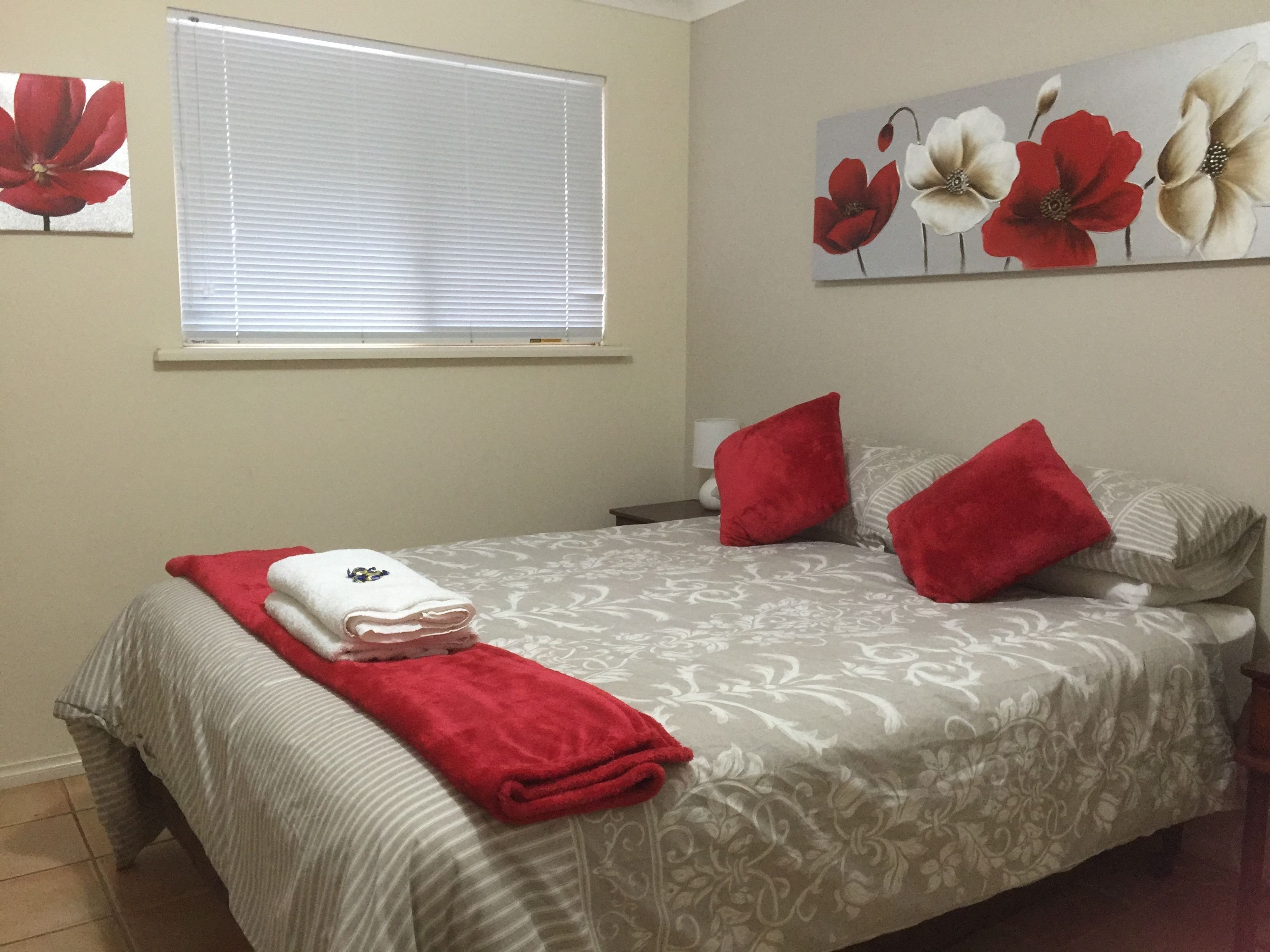 Una cama bien hecha con una colcha de estampado floral, almohadas rojas y una toalla doblada a un lado.