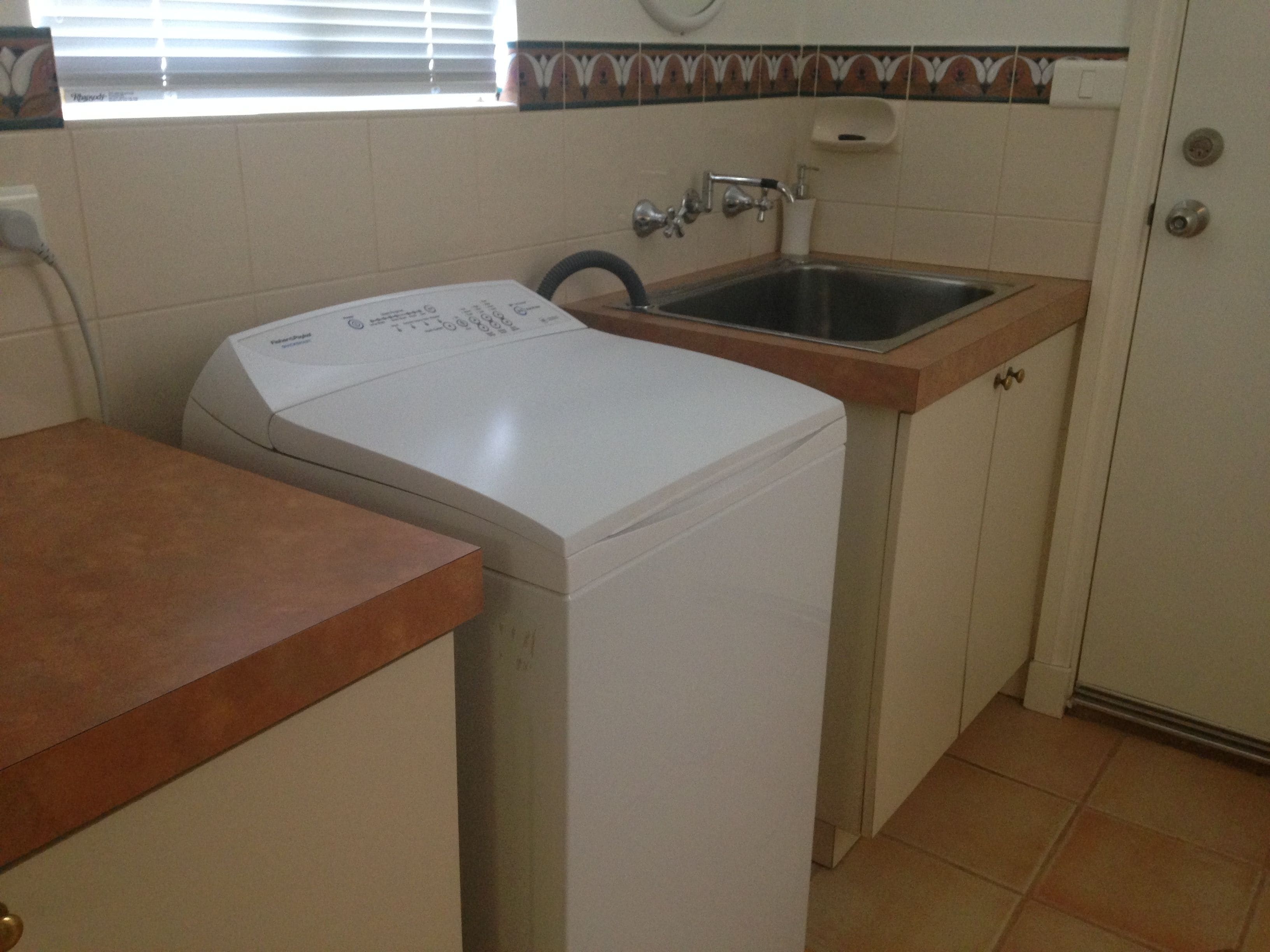 Cocina compacta con lavadora, pileta y salpicadero de azulejos.