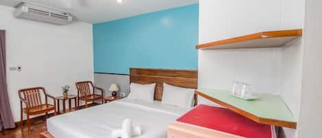 Hotelkamer met een bed, een houten hoofdeinde, een plafondventilator, een airconditioning, een kleine tafel met stoelen en een plank met glazen.