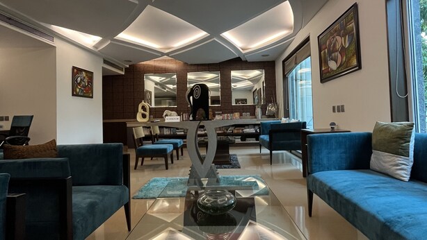 A modern living room with a glass coffee table, blue sofas, and a decorative sculpture. - YUHI MANSIONS | A Boutique Stay (Gurugram)