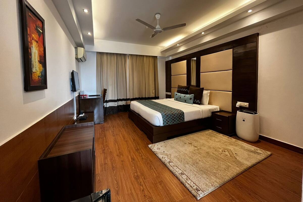 Ein modernes Hotelzimmer mit einem großen Bett, einem Schreibtisch, einem Stuhl, einem Deckenventilator und einem großen Fenster mit Vorhängen.