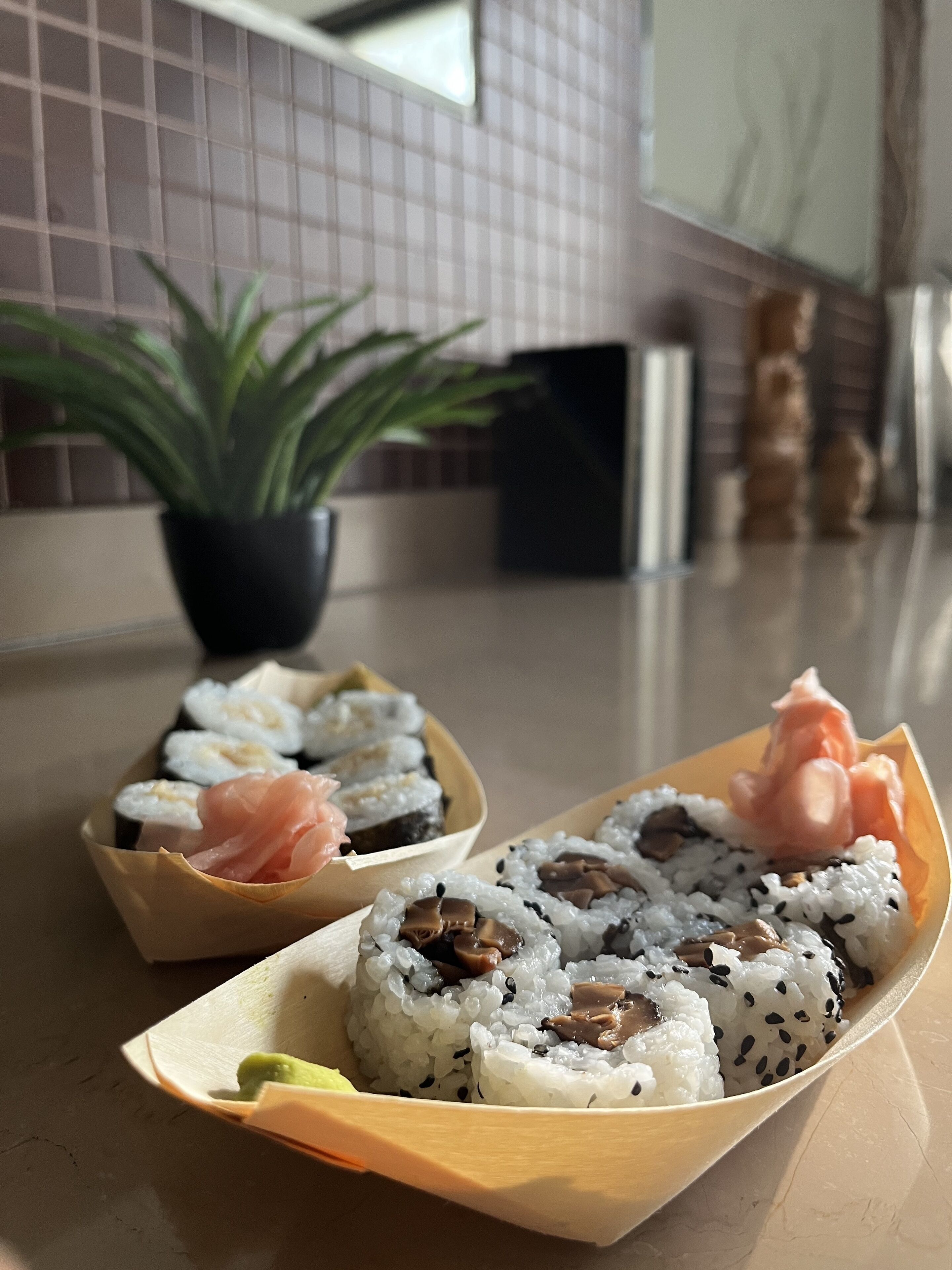 Twee schalen sushi op een aanrecht, met een plant in pot op de achtergrond.