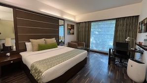 A hotel room with a large bed, a desk, a chair, and a TV. - YUHI MANSIONS | A Boutique Stay (Gurugram)