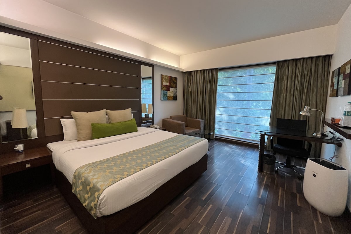 Ein Hotelzimmer mit einem großen Bett, einem Schreibtisch, einem Sessel und einem Fernseher.
