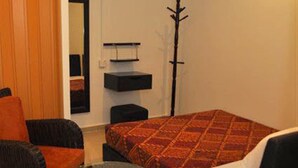 A compact room with a bed, a chair, a small table, a coat rack, and a mirror. - Old Budget Hotel (George Town)